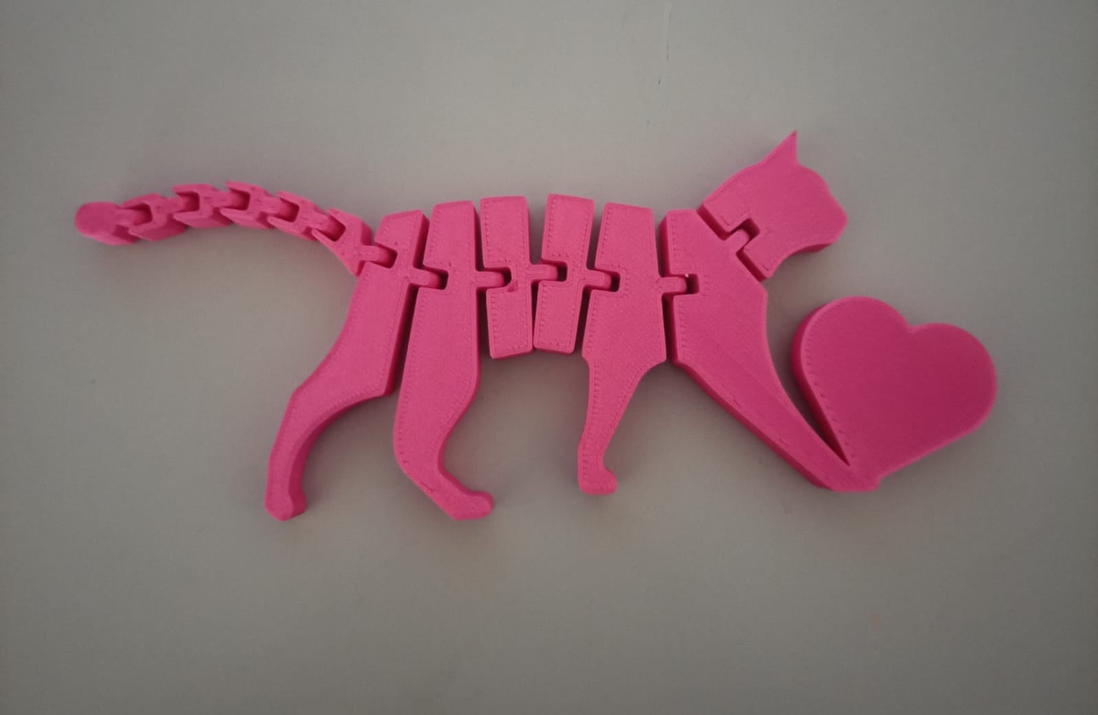 Gato articulado rosa impresso em 3D, vista superior mostrando corpo flexível e coração