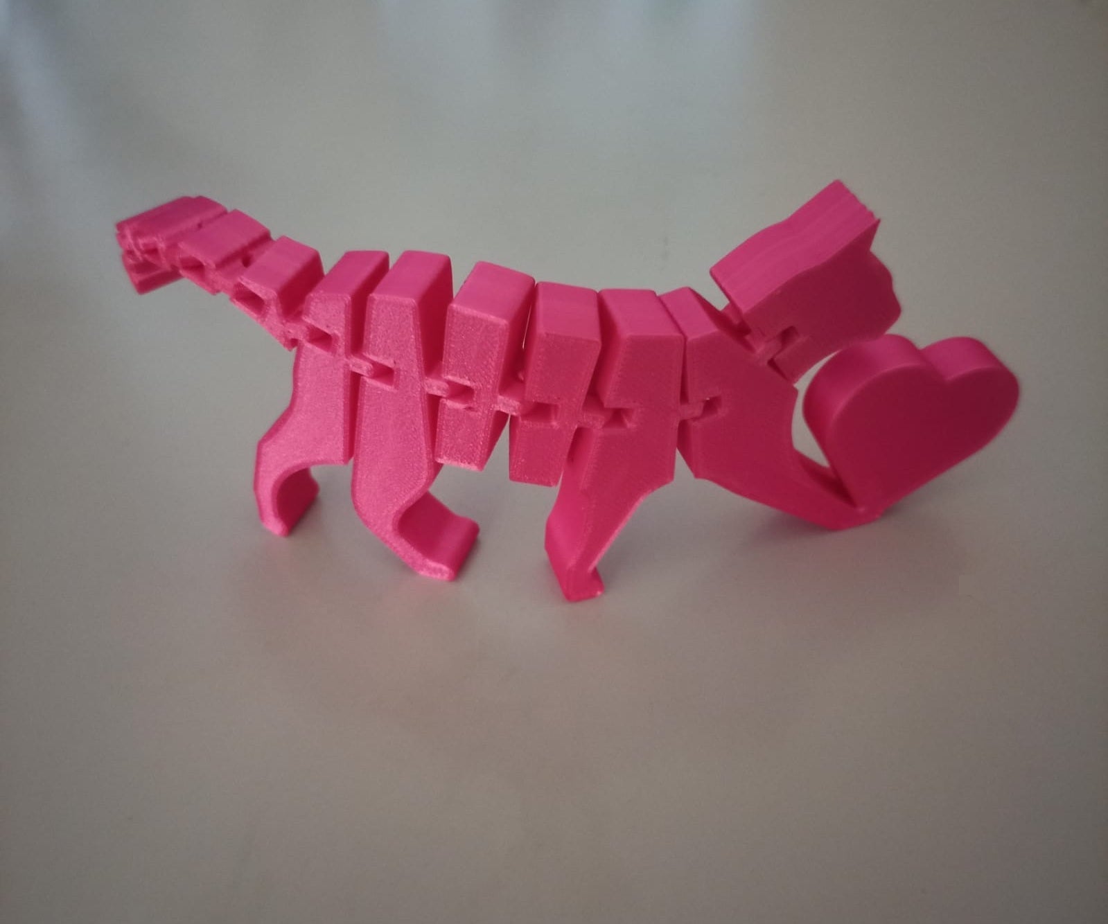 Gato articulado rosa impresso em 3D com filamento PLA, vista lateral mostrando corpo segmentado e coração na traseira