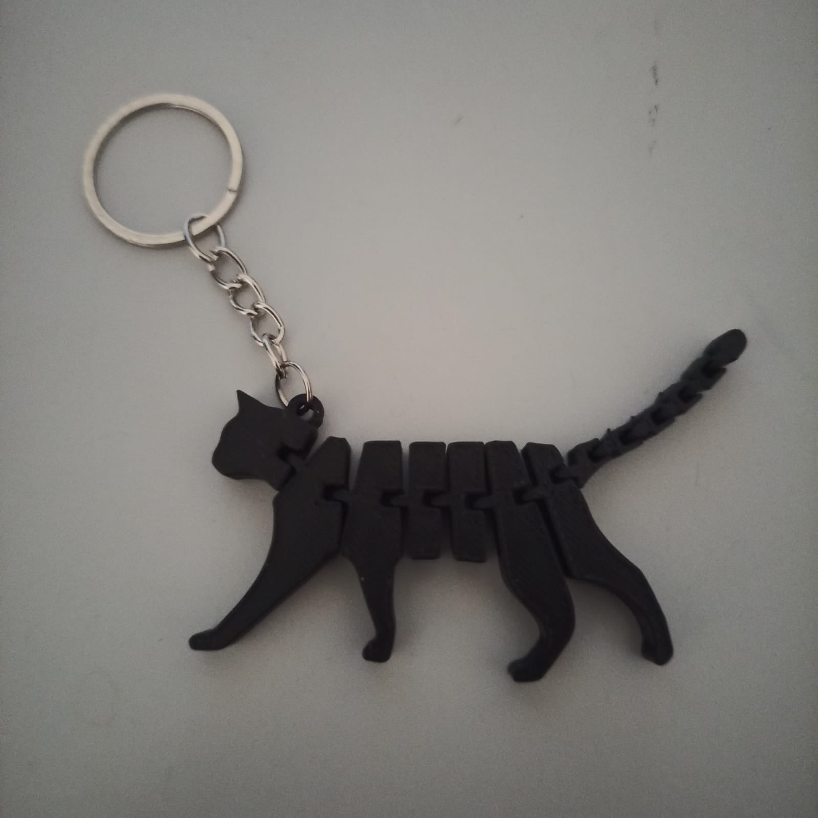 Chaveiro gato articulado impresso em 3D em filamento PLA preto, vista frontal com argola metálica